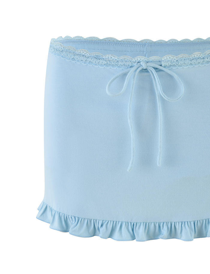 The MELLIE SKORT - BLUE by TIGERMIST is a baby blue mini skort in buttery jersey with tonal lace at the waistband, a center bow, and a ruffled hem.