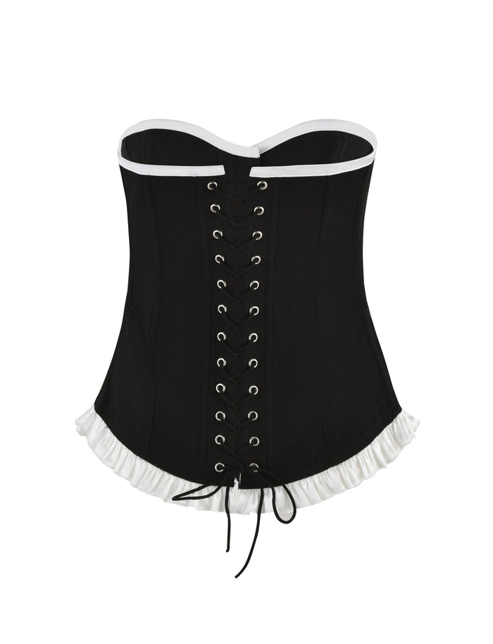Introducing the MILLIE CORSET 2.0 - BLACK by TIGERMIST: This elegant black corset is adorned with delicate white lace trim at both the top and bottom, featuring an intricate front closure with detailed black laces threaded through silver eyelets and tied in a graceful bow. For added sophistication, it also sports a chic lace-up back design.
