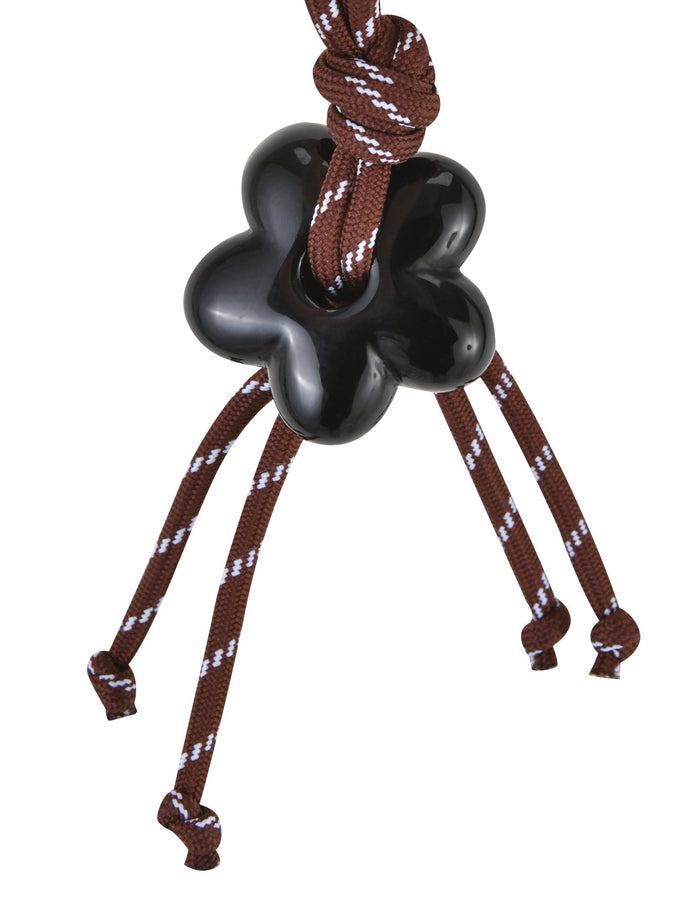 The TIGERMIST MIRIAM KEYCHAIN in chocolate features a black, flower-shaped charm on a brown cord with white patterns, elegantly extending into four knotted strands for a tassel-like look.