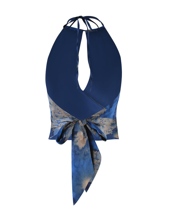 Introducing the MONROE TOP - BLUE : FLORAL by TIGERMIST, a chic sleeveless halter top showcasing a deep V-neck and a waist-knot design. The fabric is adorned with a blue tie-dye pattern, resembling a floral watercolor print with subtle gradients that blend seamlessly for an elegant and modern aesthetic.