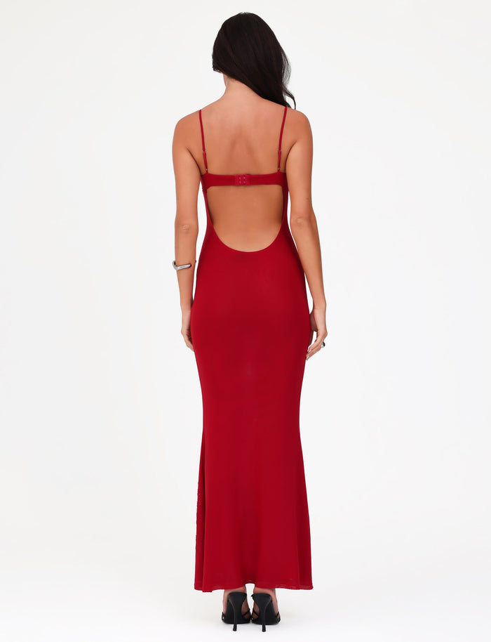 A woman, with her back to the camera, elegantly displays the exquisite OCTAVIA MAXI DRESS in Cherry Red by TIGERMIST. This backless dress boasts thin straps and delicate floral embellishments. Her long hair drapes over her shoulders, while black high-heeled shoes complete her ensemble against a plain white backdrop.