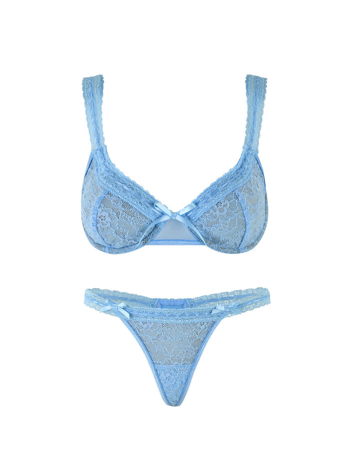 The PANDORA SET - BLUE by TIGERMIST is a matching ensemble of light blue lace lingerie, featuring intricate lace detailing and small satin bows at the center of the bra. The thong, made with sheer mesh and complementary patterns, also has a matching bow at the front. Both pieces are delicate and feminine in design.