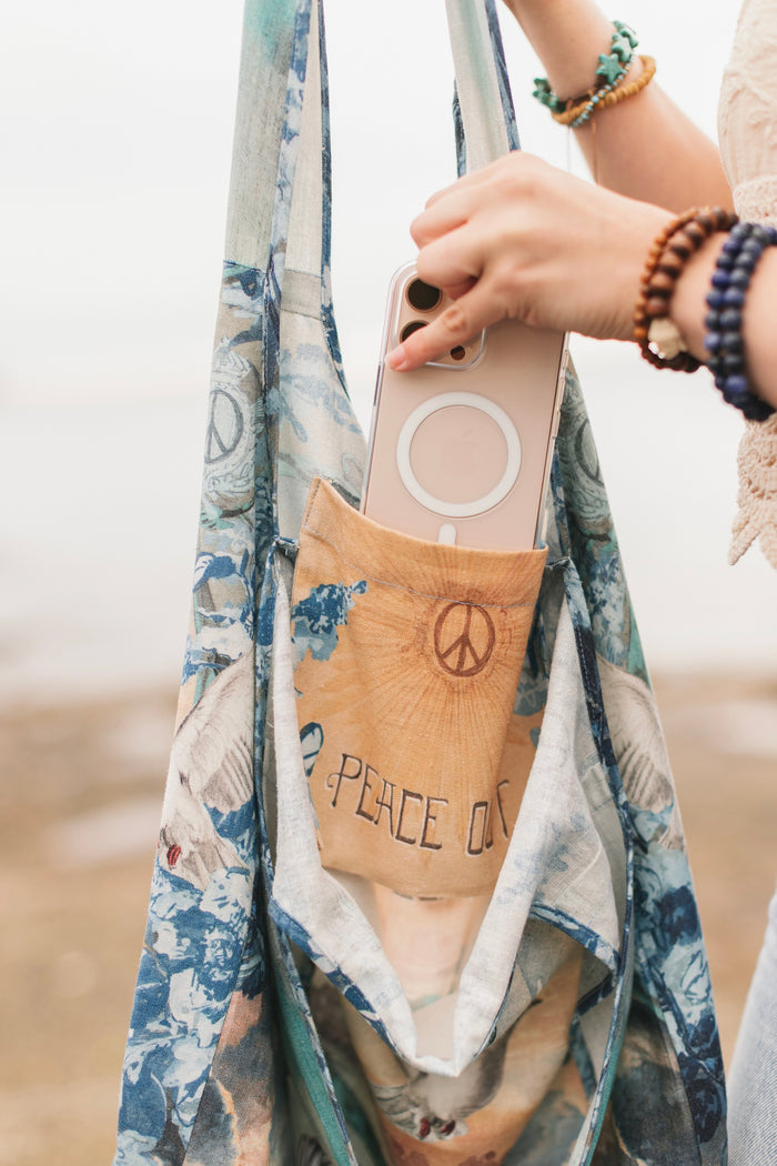 Model wearing our Peace Out tote bag featuring 1800's perfumeur sign with gentle tones of blue & aqua, landscapes, clouds, dove, and peace symbols -Market of Stars.