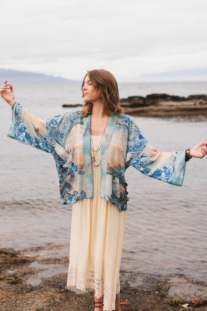 Model wearing our Peace Out Pixie Duster featuring 1800's perfumeur sign with gentle tones of blue & aqua, landscapes, clouds, dove and peace symbols -Market of Stars.