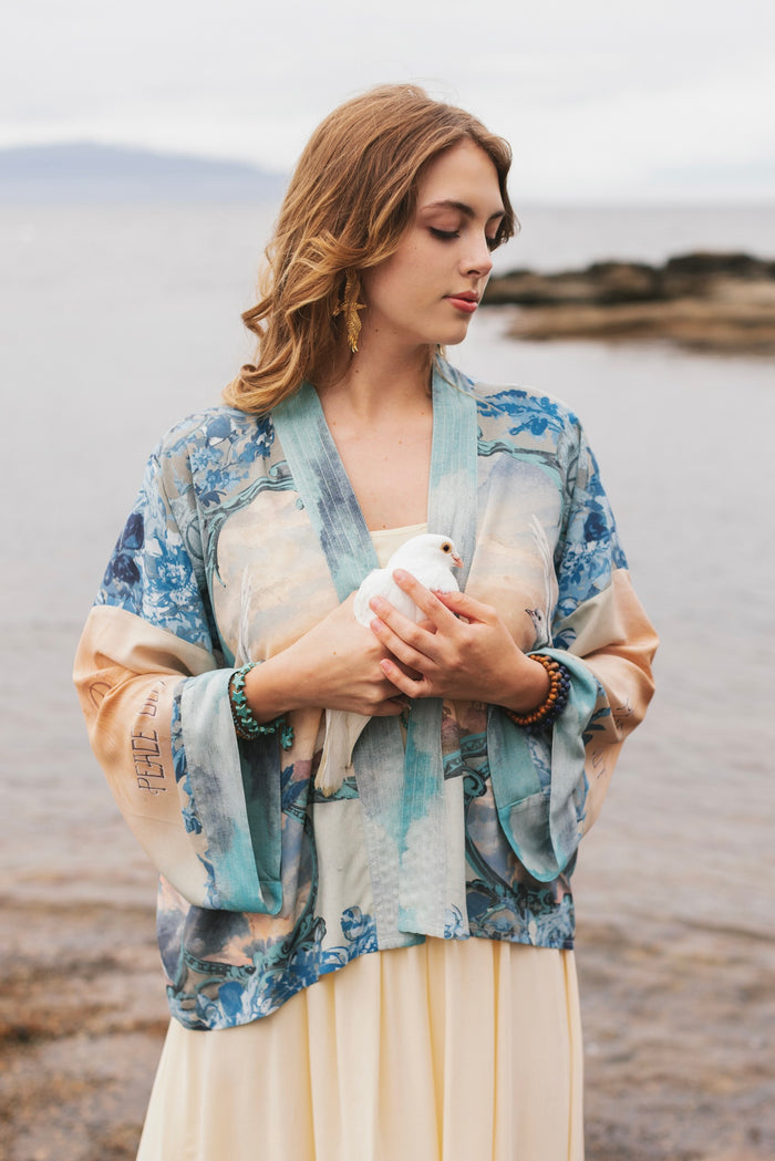 Model wearing our Peace Out Pixie Duster featuring 1800's perfumeur sign with gentle tones of blue & aqua, landscapes, clouds, dove and peace symbols -Market of Stars.