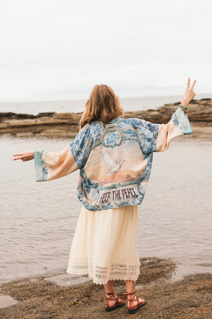Model wearing our Peace Out Pixie Duster featuring 1800's perfumeur sign with gentle tones of blue & aqua, landscapes, clouds, dove and peace symbols -Market of Stars.