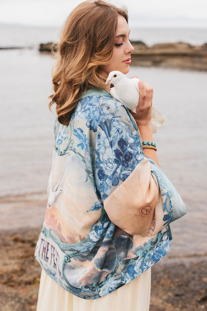 Model wearing our Peace Out Pixie Duster featuring 1800's perfumeur sign with gentle tones of blue & aqua, landscapes, clouds, dove and peace symbols -Market of Stars.