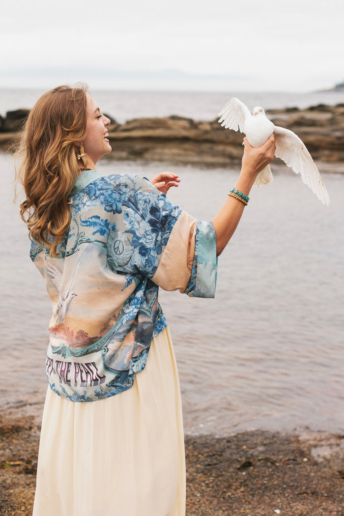 Model wearing our Peace Out Pixie Duster featuring 1800's perfumeur sign with gentle tones of blue & aqua, landscapes, clouds, dove and peace symbols -Market of Stars.