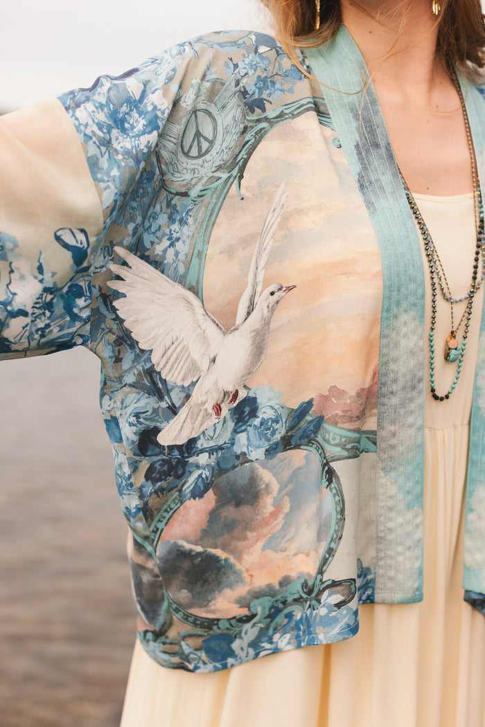 Model wearing our Peace Out Pixie Duster featuring 1800's perfumeur sign with gentle tones of blue & aqua, landscapes, clouds, dove and peace symbols -Market of Stars.