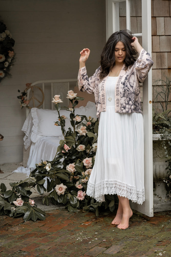 Model wearing Peace, Wine & Sunshine Bohéme Slip Dress featuring botanical collages and playful peace, wine and sunshine lettering on the hem – Market of Stars.