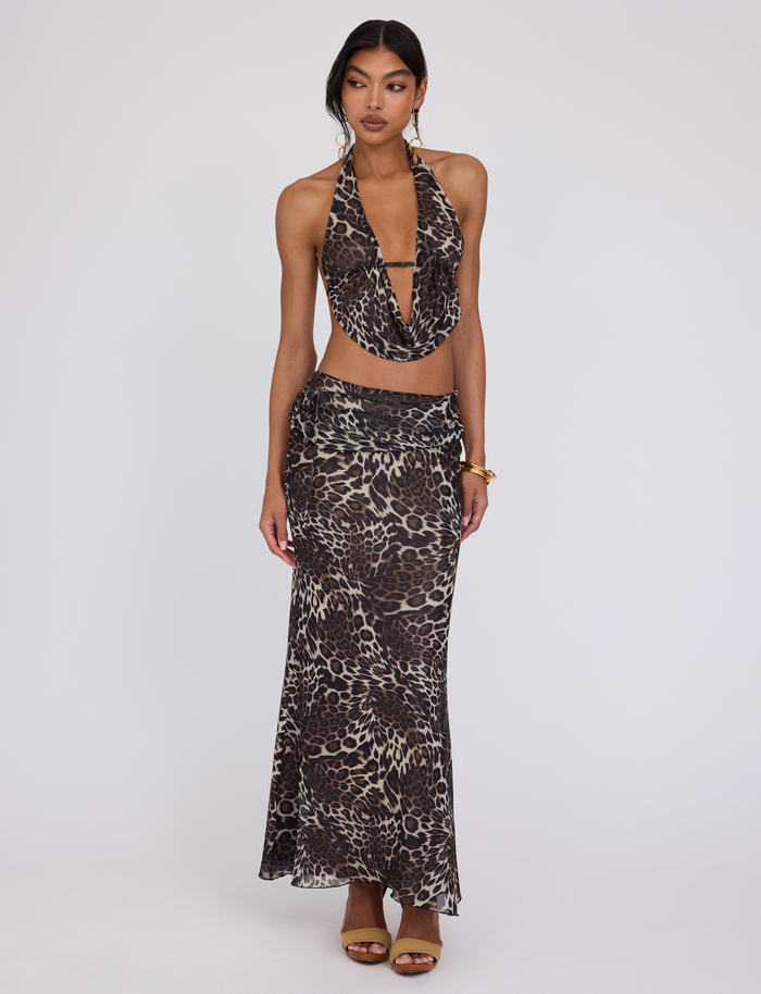 A woman poses against a plain background wearing the TIGERMIST PEARL MAXI SKIRT - MULTI : LEOPARD with a matching halter-neck top, styled with gold earrings, a bracelet, and brown high-heeled sandals.