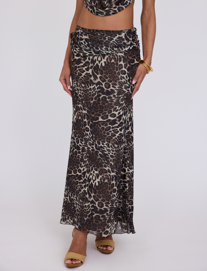 A person wears the TIGERMIST PEARL MAXI SKIRT - MULTI: LEOPARD with a matching crop top, gold bangles, and tan open-toe sandals against a plain white background.