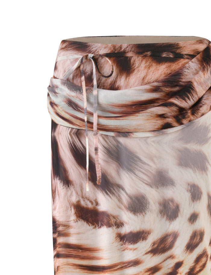 A detailed view of the TIGERMIST PEARL MAXI SKIRT - NEUTRAL : LEOPARD : LEOPARD HAZE highlights its relaxed silhouette, enhanced by draped fabric. The skirt is tied with a thin ribbon at the waist and showcases a sophisticated blend of brown, tan, and cream hues in its leopard pattern.