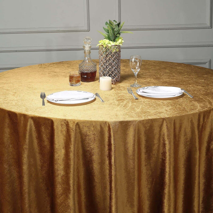 Elegant round table set with gold tablecloth, plates, and decorative items.