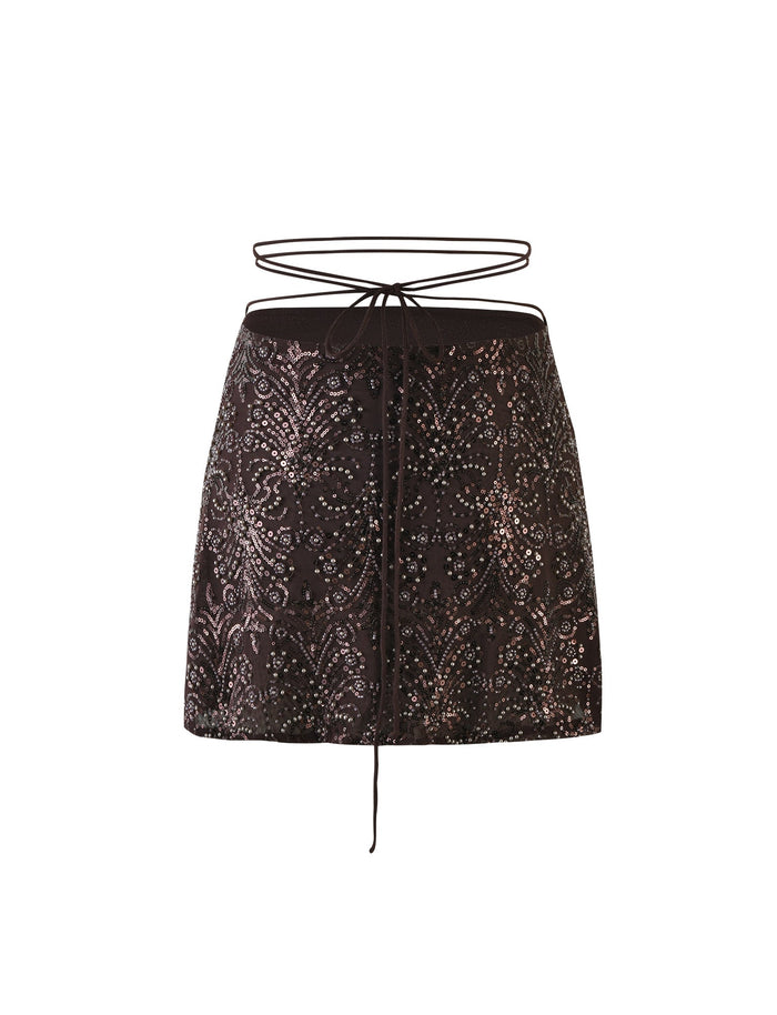 A chocolate mini skirt by TIGERMIST adorned with intricate sequin embroidery, featuring a lace-up waist detail with thin straps tied in a bow at the front. The decorative pattern includes swirling floral designs, adding a touch of elegance and sparkle to the RAINA SKIRT.