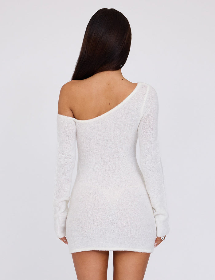 A person with long brown hair is facing away from the camera, wearing the TIGERMIST RYKER DRESS in white and cream. The dress is a fuzzy, off-shoulder mini dress with long sleeves and an asymmetrical neckline that reveals one shoulder. The background is plain white.
