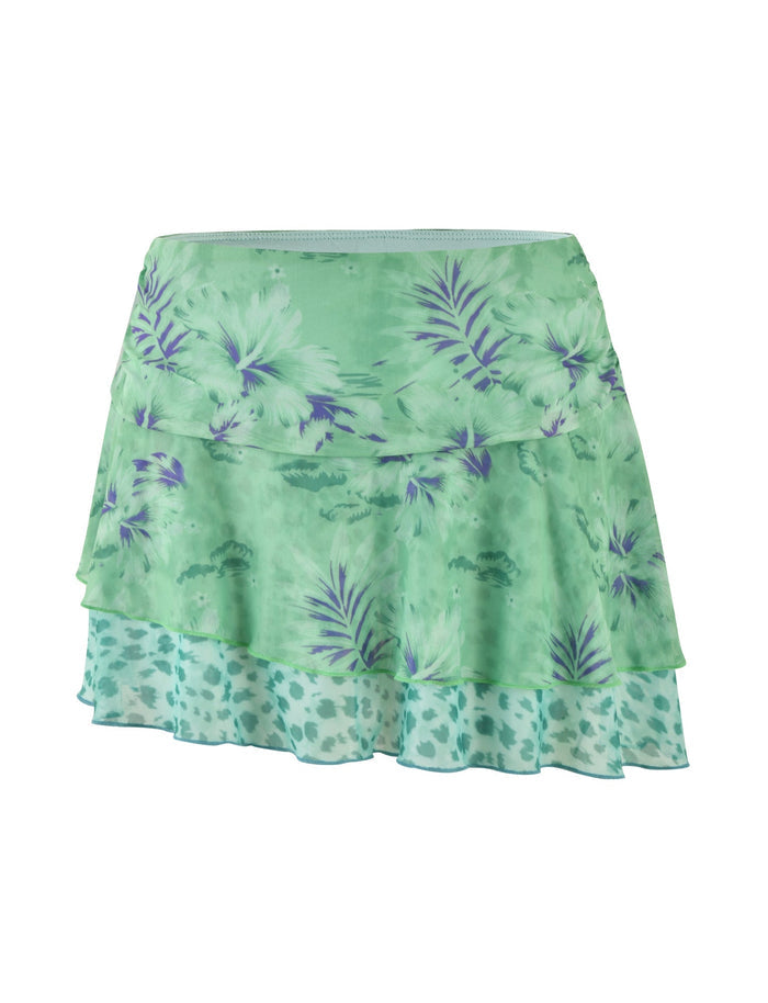 Introducing the SAIGE SKIRT by TIGERMIST, a stylish light green skirt featuring purple floral patterns and a tiered design. The bottom tier showcases a semi-sheer fabric with leopard-like spots, effortlessly blending floral and animal prints for an exquisite layered, textured appearance. Made from high-stretch fabric and equipped with an elastic waistband, it ensures ultimate comfort and an impeccable fit.