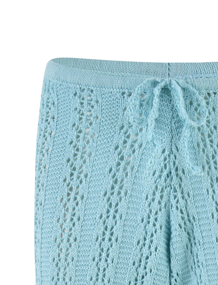 Close-up of the SANDOR PANT - BLUE : BABY BLUE by TIGERMIST showcasing a drawstring waistband. The fabric features a delicate, lacy pattern with small holes, adding an intricate texture to the garment. The knit appears soft and slightly stretchy.