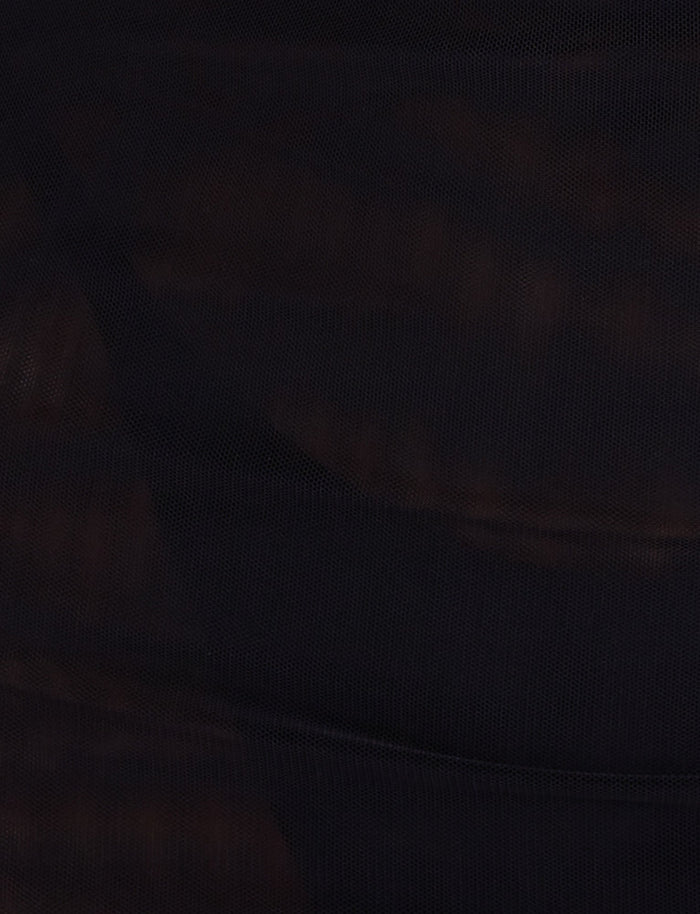 A close-up of the dark, textured fabric on the SONORA MINI DRESS - BLACK by TIGERMIST. The material appears slightly sheer with a subtle checkered pattern, creating a mix of shadowy and translucent areas across the surface. Chain detailing adds to the moody and mysterious atmosphere enhanced by the lighting.
