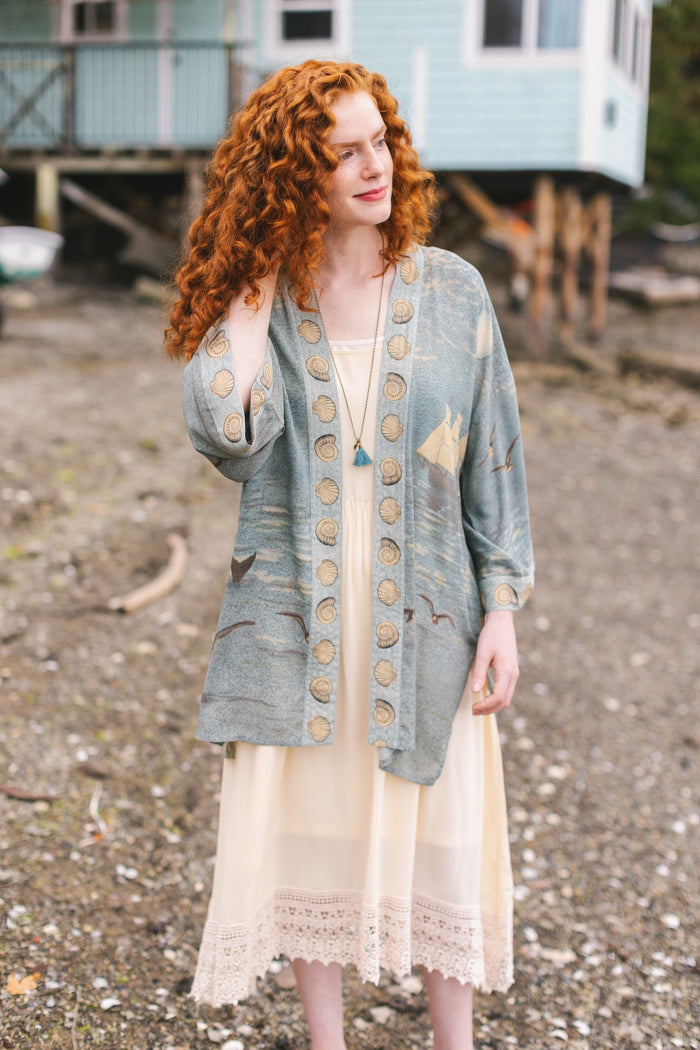 Lightweight duster featuring antique sunrise sky, mermaid, shell, and soaring birds artwork, shown on model at the beach – Market of Stars