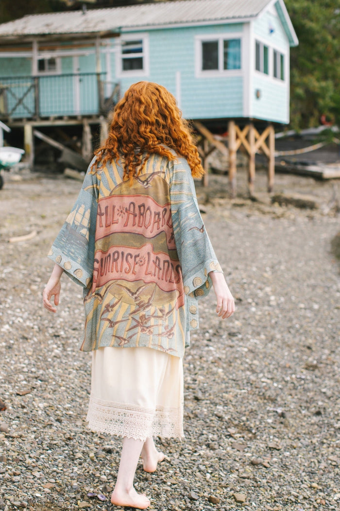 Lightweight duster featuring antique sunrise sky, mermaid, shell, and soaring birds artwork, shown on model at the beach – Market of Stars