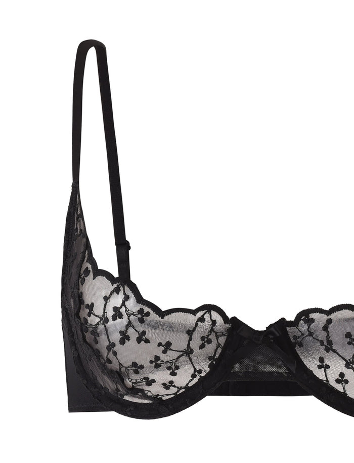 A TALIYAH SET - BLACK by TIGERMIST is shown, featuring a black lace bra with scalloped edges and floral embroidery. The underwire cup design offers excellent support, while adjustable shoulder straps and a small bow at the center of the front band add delicate touches.