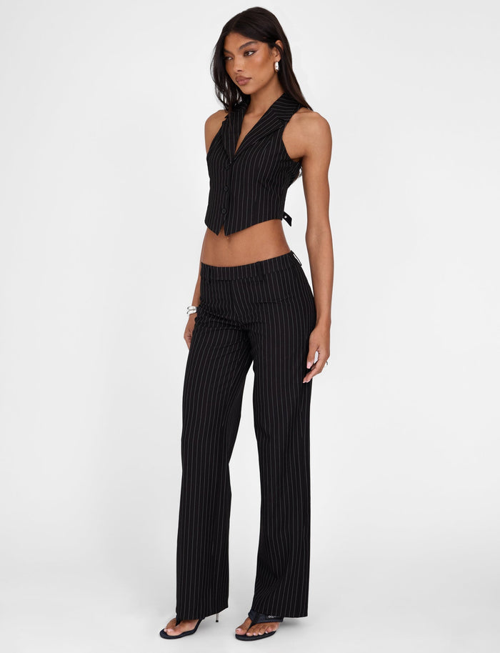 A woman is modeling a stylish two-piece outfit from TIGERMIST, featuring the TAMARA PANT - BLACK : PINSTRIPE and a matching sleeveless crop top with a collar. She completes the look with black high-heeled sandals and minimal jewelry, standing against a plain white background.