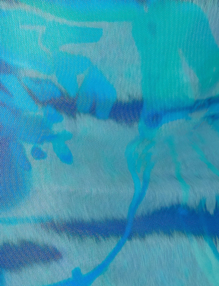 A close-up view of the TENLEY DRESS - MULTI : ABSTRACT TIE DYE by TIGERMIST showcases its vibrant abstract pattern in shades of blue, teal, and white. The design features brushstroke-like textures and fluid shapes, creating a dynamic and visually engaging composition.