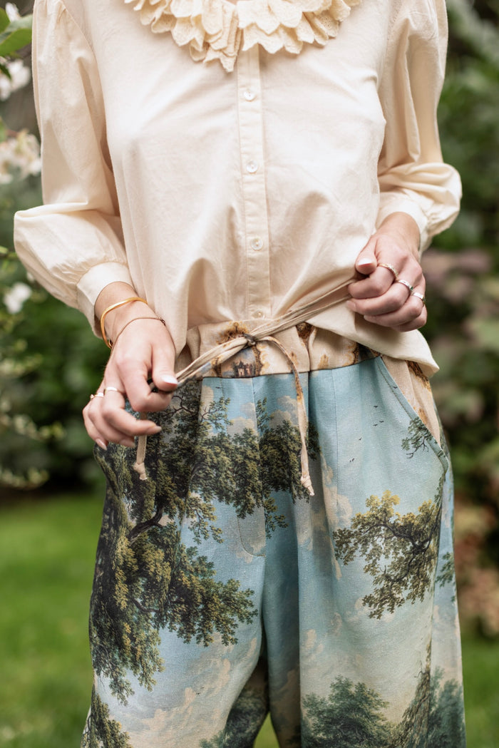 Model wearing a cropped length linen blend pant ft. vintage artwork & unicorn lorn set against a mossy-green landscape — a romantic piece for the modern dreamer - Market of Stars