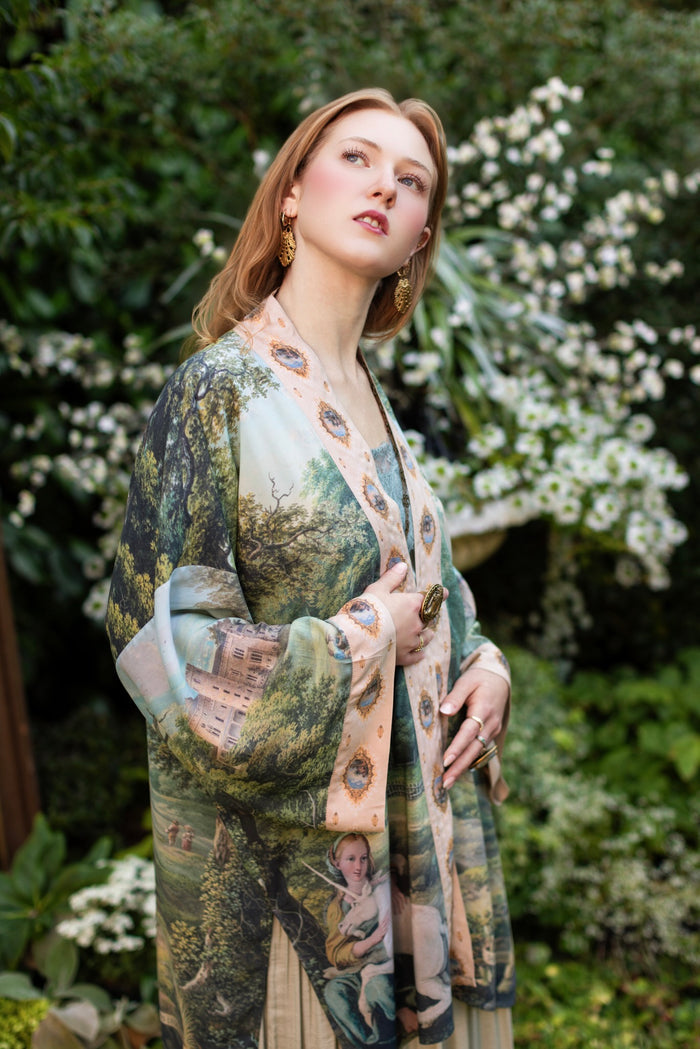 Model wearing a mid-length duster ft. vintage artwork & unicorn lorn set against a mossy-green landscape — a romantic piece for the modern dreamer - Market of Stars