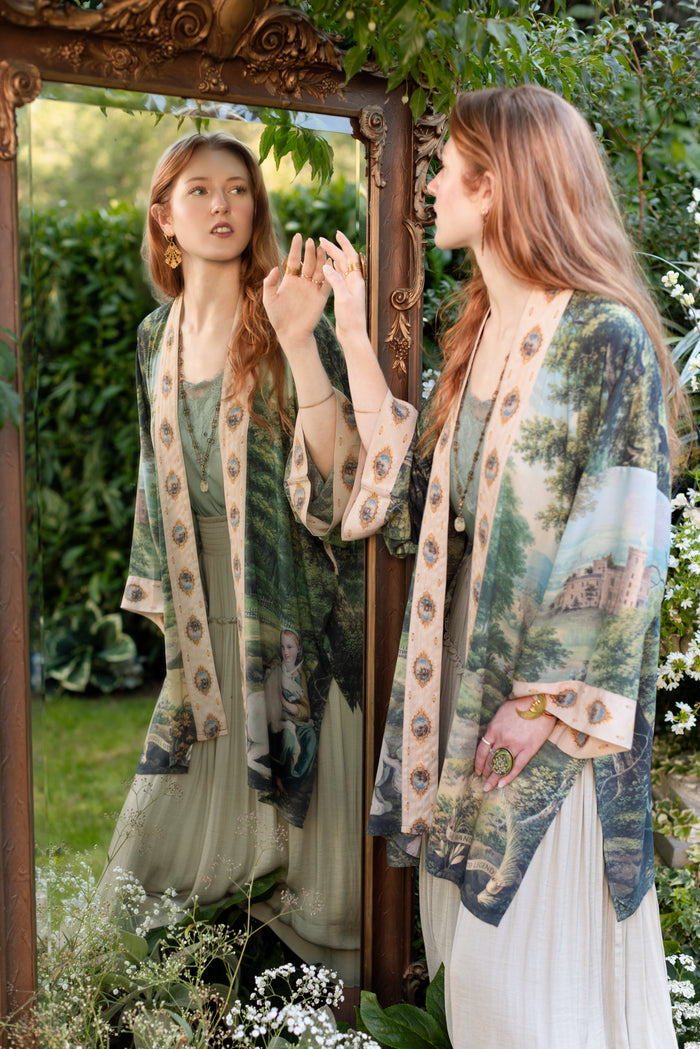 Model wearing a mid-length duster ft. vintage artwork & unicorn lorn set against a mossy-green landscape — a romantic piece for the modern dreamer - Market of Stars