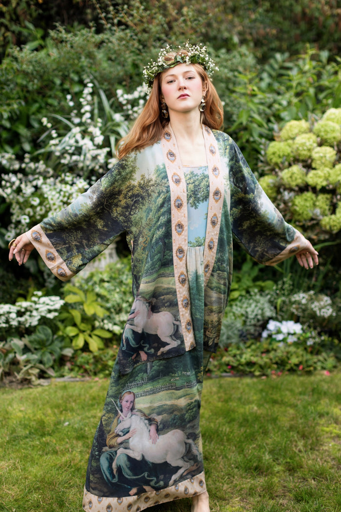 Model wearing a mid-length duster ft. vintage artwork & unicorn lorn set against a mossy-green landscape — a romantic piece for the modern dreamer - Market of Stars