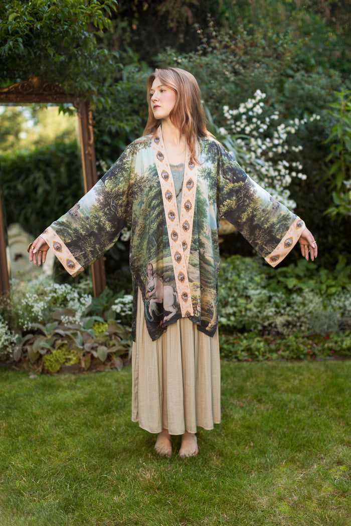 Model wearing a mid-length duster ft. vintage artwork & unicorn lorn set against a mossy-green landscape — a romantic piece for the modern dreamer - Market of Stars