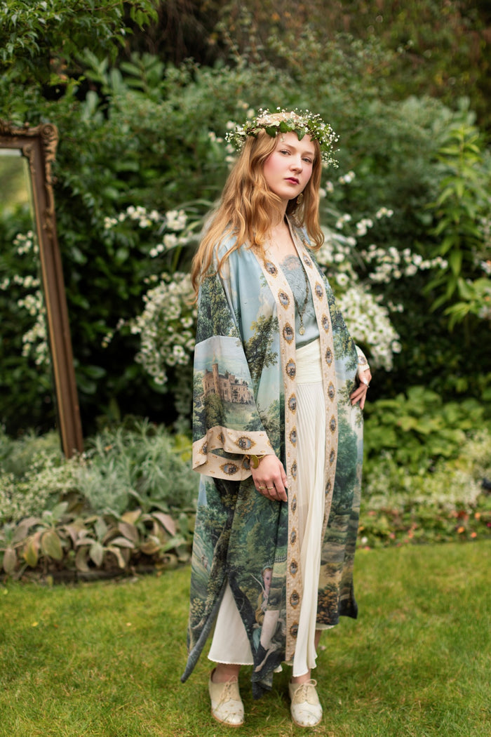 Model wearing a full-length duster ft. vintage artwork & unicorn lorn set against a mossy-green landscape — a romantic piece for the modern dreamer - Market of Stars