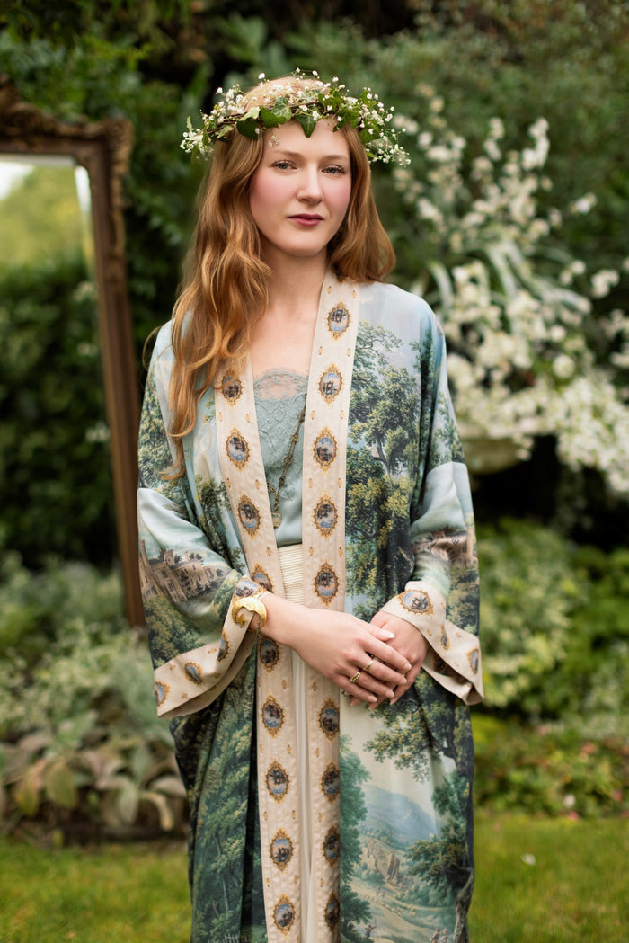 Model wearing a full-length duster ft. vintage artwork & unicorn lorn set against a mossy-green landscape — a romantic piece for the modern dreamer - Market of Stars