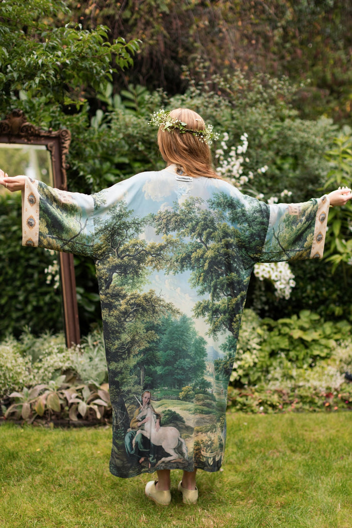 Model wearing a full-length duster ft. vintage artwork & unicorn lorn set against a mossy-green landscape — a romantic piece for the modern dreamer - Market of Stars