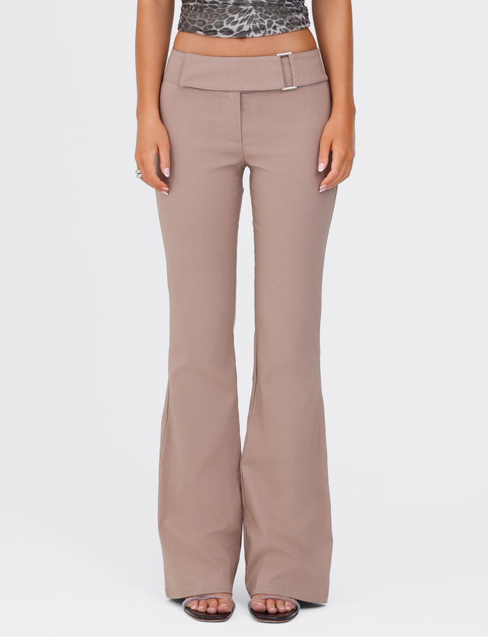A person wearing the VESPER PANT in Brown Tan by TIGERMIST, featuring flared legs, a high waist, and a belt buckle detail. Paired with an animal print top, the individual stands with their hands relaxed at their sides, exuding a polished yet casual style.