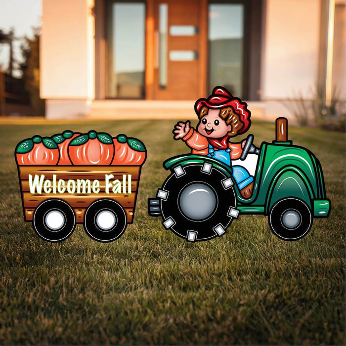 A yard decoration featuring a cartoon of a boy driving a green tractor with a cart of pumpkins, and the text 'Welcome Fall' displayed.