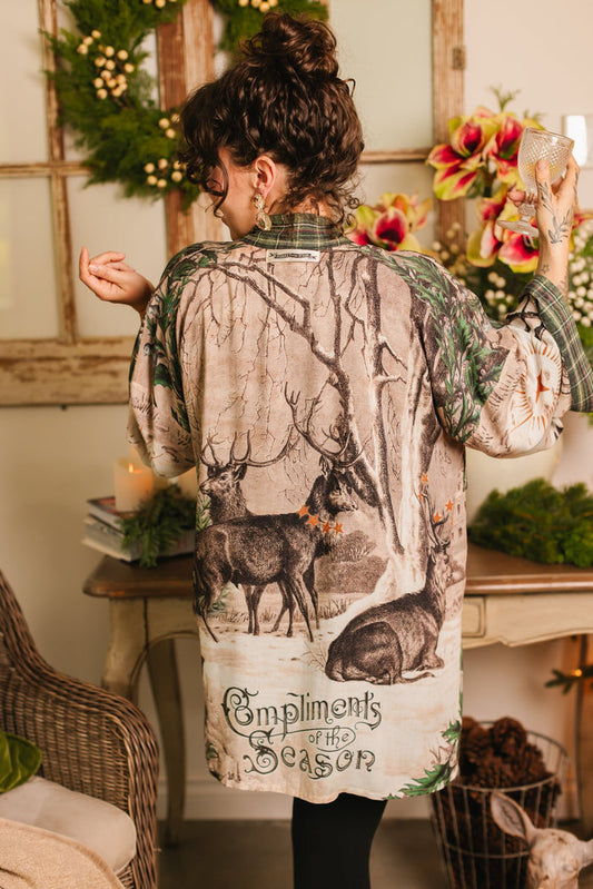 Model wearing a bamboo viscose mid-length duster with Victorian-era images from holiday greeting cards — including reindeer in the snow, a little fir tree, golden stars, and traditional plaid trim - Market of Stars