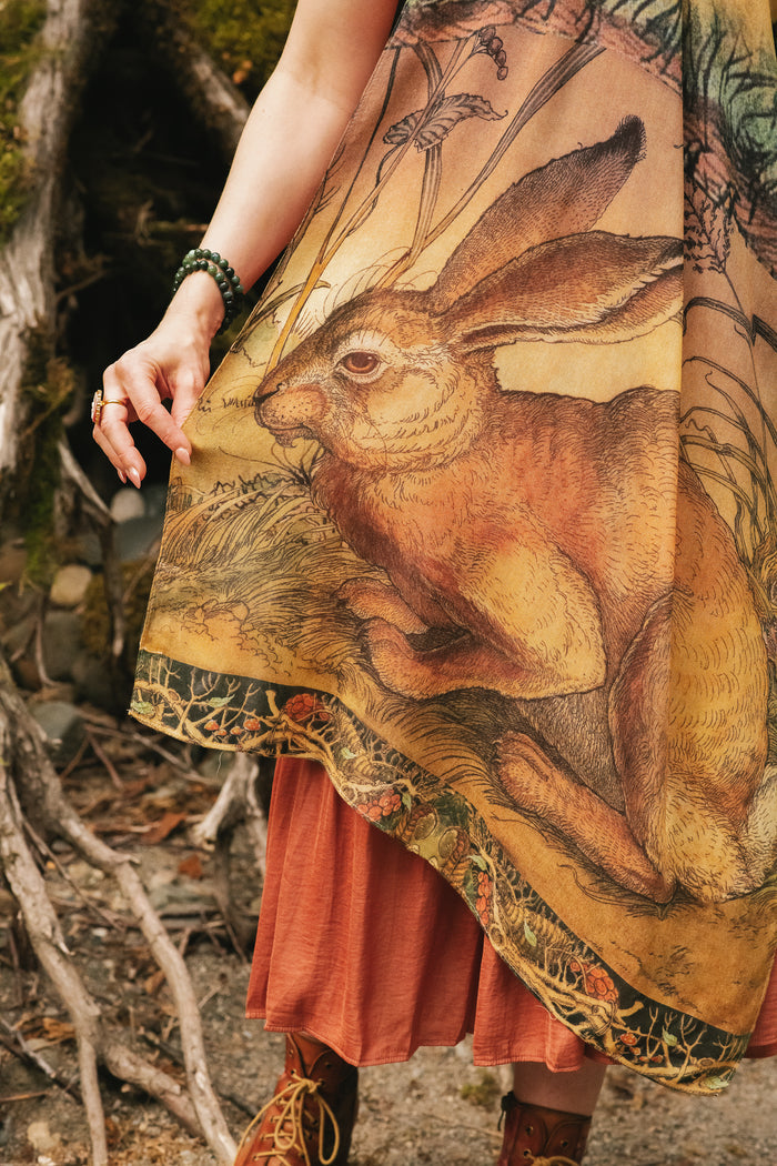 Model wearing a bamboo-viscose scarf where a noble rabbit rests deep within an underground burrow, surrounded by the warmth and safety of the earth. Created in collaboration with Charles van Sandwyck - Market of Stars