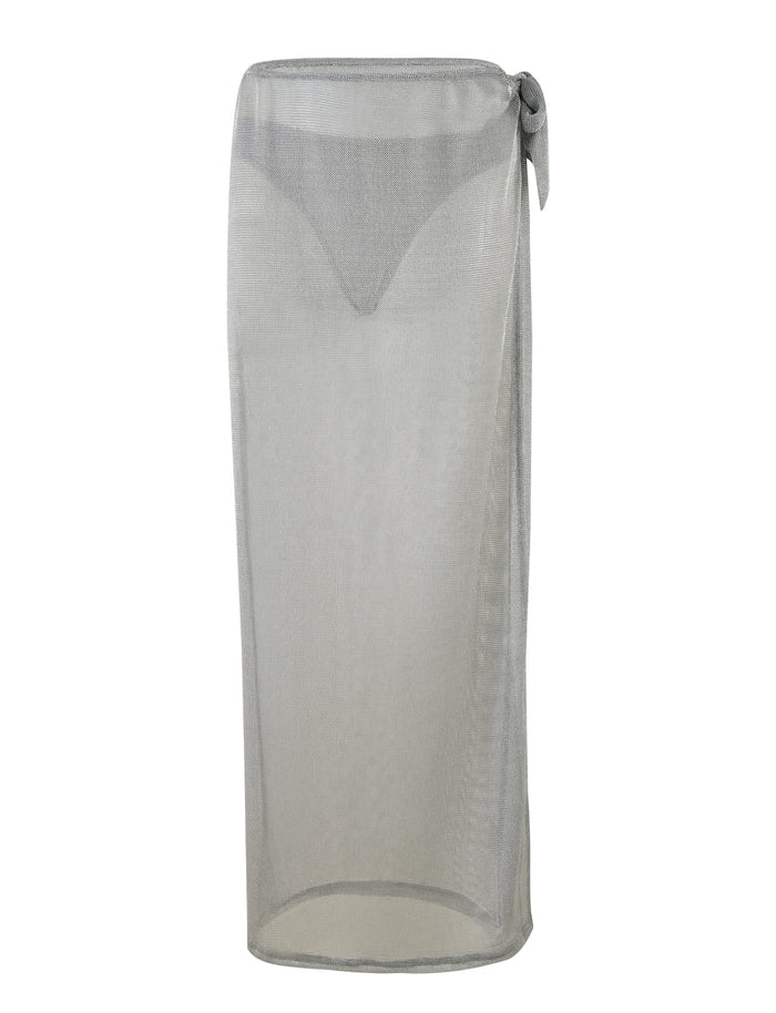 A sheer, lightweight WYNNE SKIRT - GREY : SILVER from TIGERMIST, tied at a low-rise waist with a knot on the right side. This mid-length skirt extends down to the calves and is semi-transparent, revealing the silhouette of a bikini underneath.
